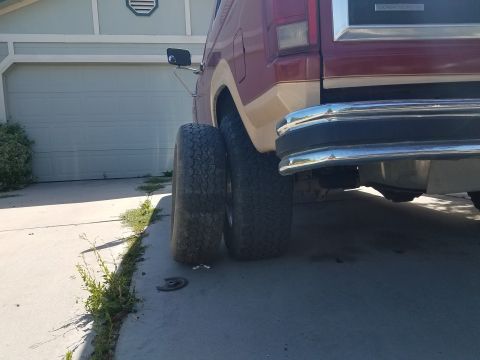 1985 Ford Bronco - Rear view of a red and tan Ford Bronco with large tires parked in front of a garage.