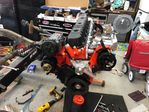 1992 Jeep Wrangler - Engine assembly with orange block and black valve cover sits on a workshop floor with tools and a red wagon nearby.