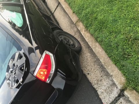 2008 Ford Focus - Rear view of a damaged black car with a detached hubcap, parked next to a curb.