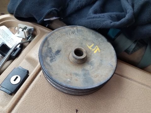 1985 Ford Bronco - Pulley part with stamped numbers and yellow markings sits on a vehicle's dashboard.