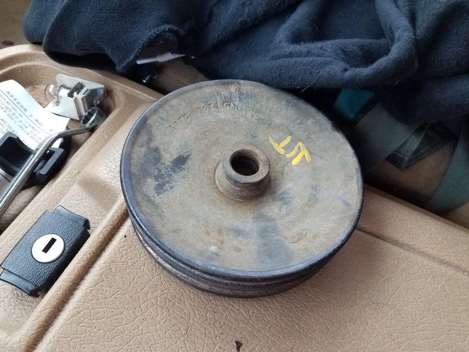 Pulley with part number 2775 10073 GA stamped on it, sitting on a tan dashboard