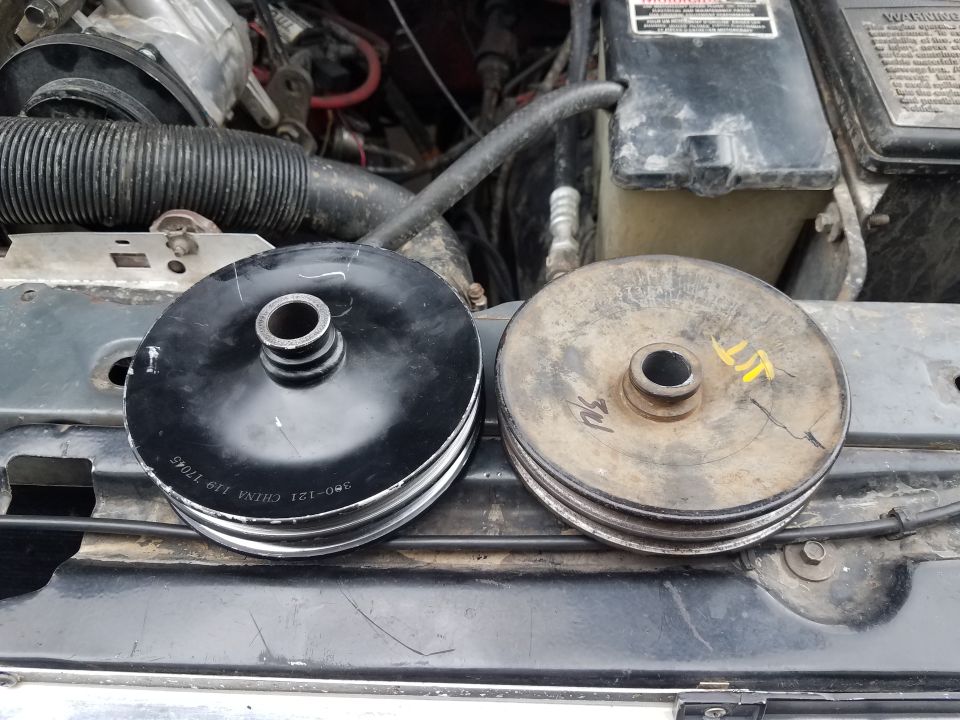 New black pulley next to a worn, cracked pulley. Engine parts visible in background