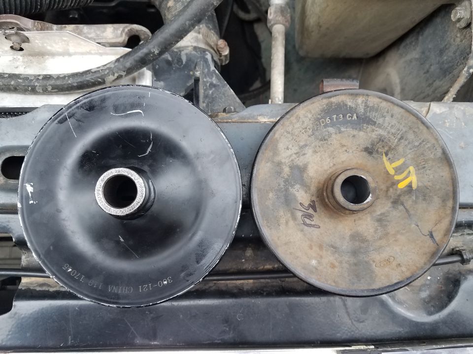 Two pulleys, one black and new, the other rusty and used, sit side-by-side in an engine bay