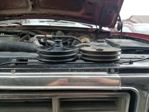 1985 Ford Bronco - Two engine pulleys are displayed on the grille of a vehicle with the hood open, revealing the engine compartment.