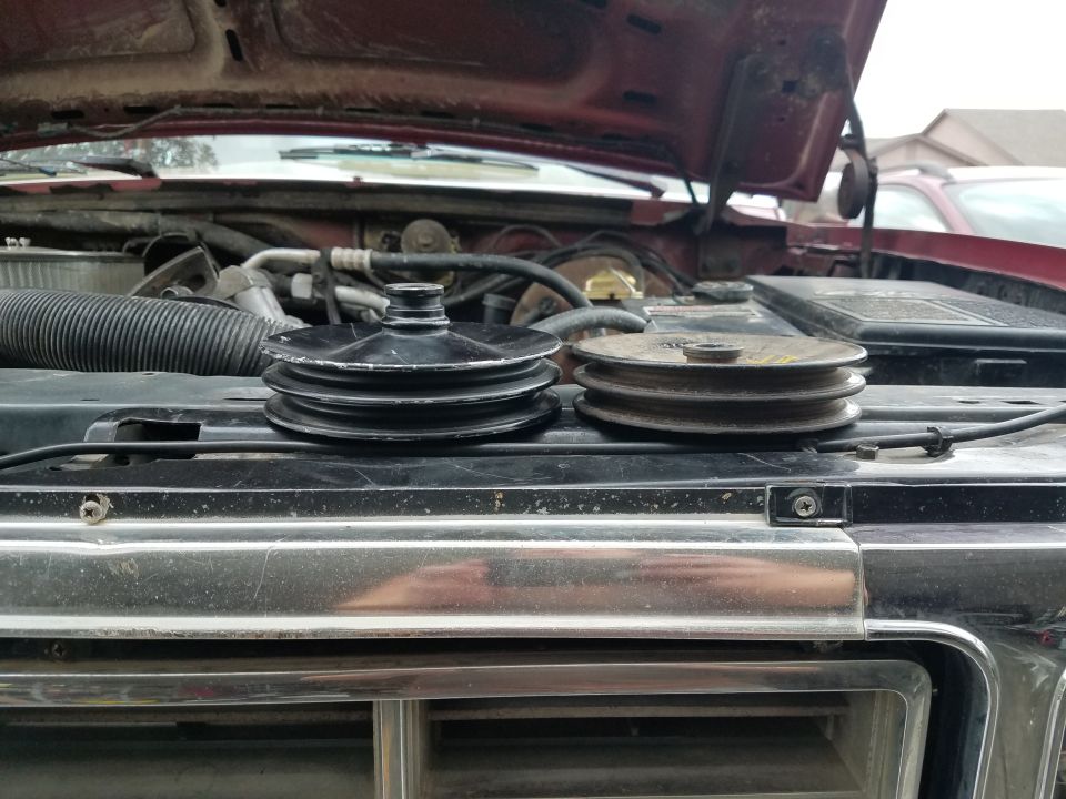 Two engine pulleys on a vehicle grille, one black and one rusty