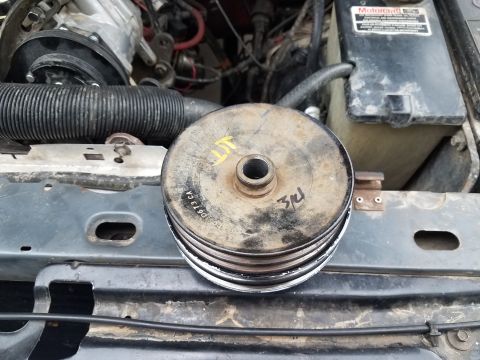 1985 Ford Bronco - A pulley assembly sits on the engine bay of a vehicle, with handwritten markings and a partial part number visible.