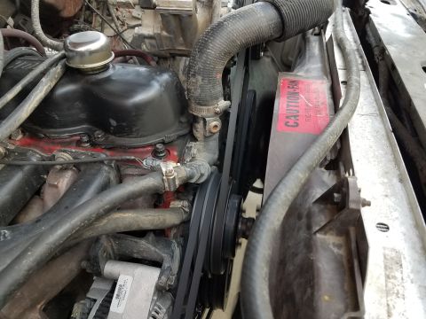 1985 Ford Bronco - Close-up view of the engine bay, showing the radiator, fan, and associated hoses and belts. A caution sticker is affixed to the fan shroud.