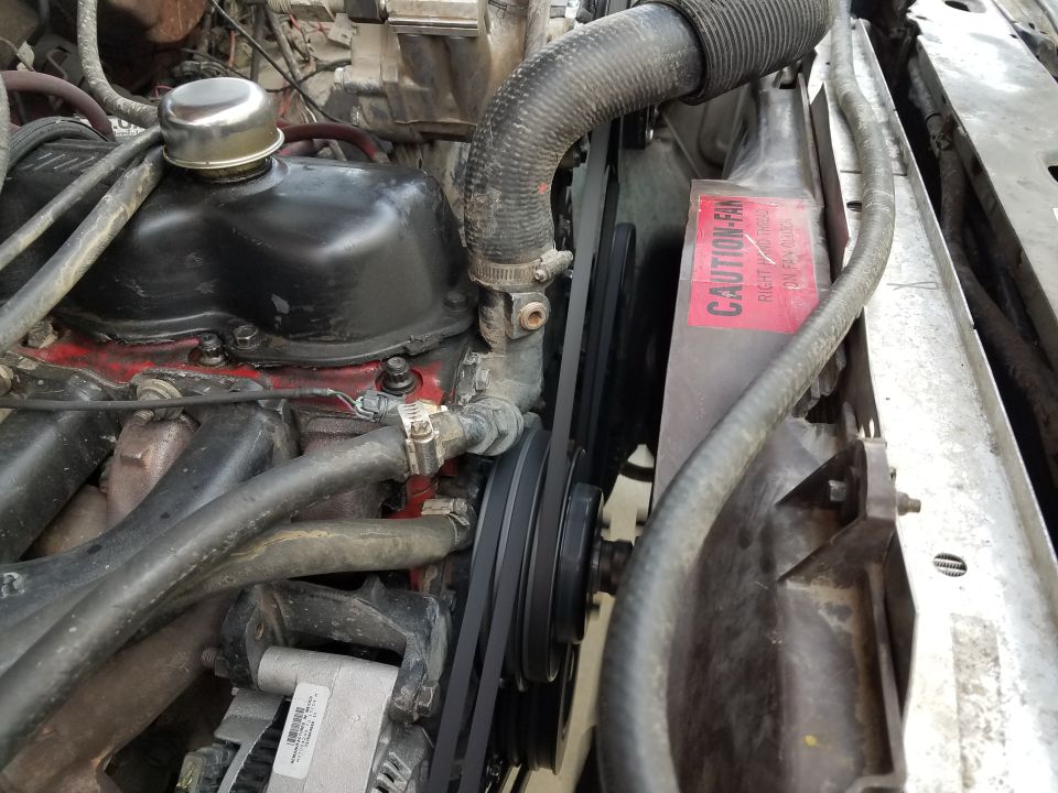 Engine bay with radiator, fan, and belts. Red 'CAUTION-FAN' sticker visible