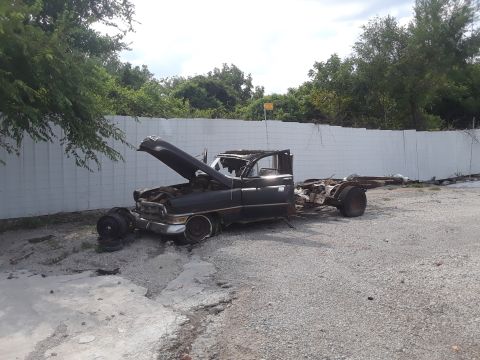 1994 Ford Bronco - This heavily damaged truck chassis, likely from the 1950s, sits abandoned with its hood open.