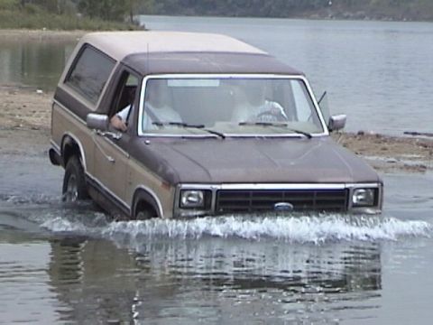 1995 Ford Bronco - Ford Bronco navigates shallow water with two occupants visible inside.