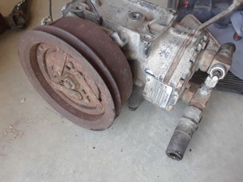 1994 Ford Bronco - A close-up view of a worn air conditioning compressor, showing its pulley and a manufacturer's tag.