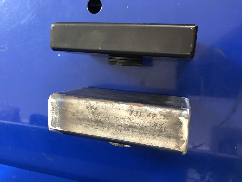 Two metal rectangular parts, one black and one silver, resting on a blue surface