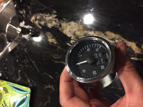 2000 Lotus Esprit - A VDO turbo gauge is held in a hand against a dark, speckled countertop.
