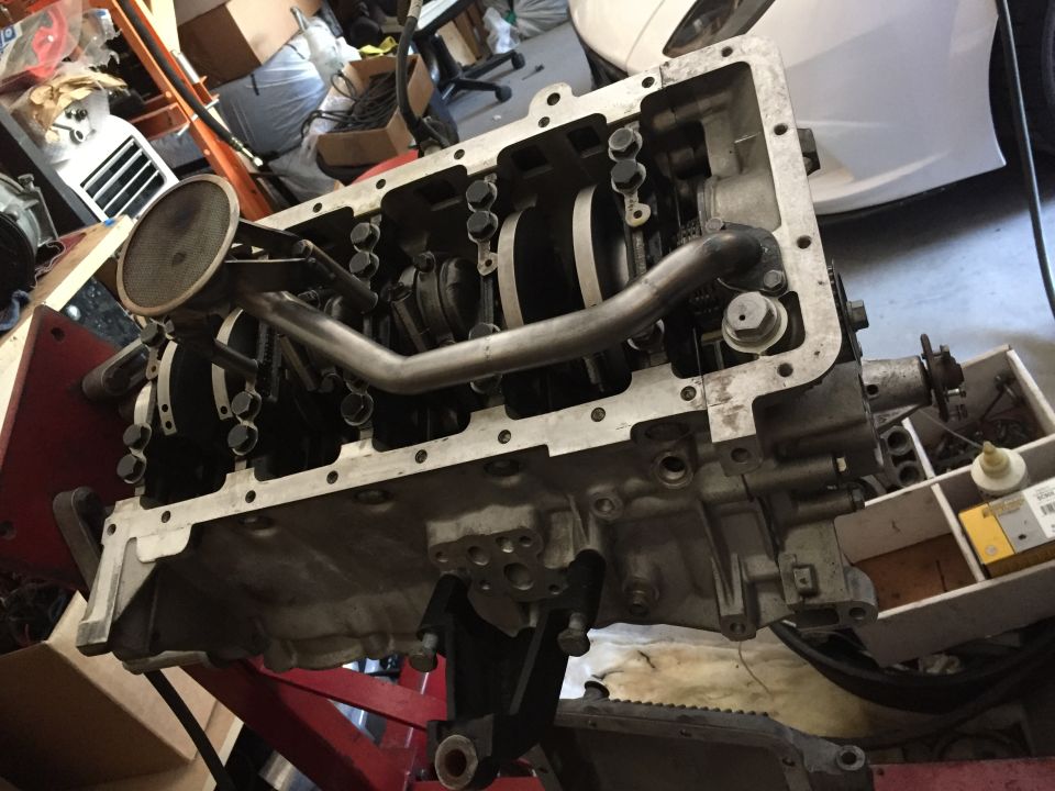 Engine block assembly with crankshaft, connecting rods, and oil pump visible. Mounted on a red stand