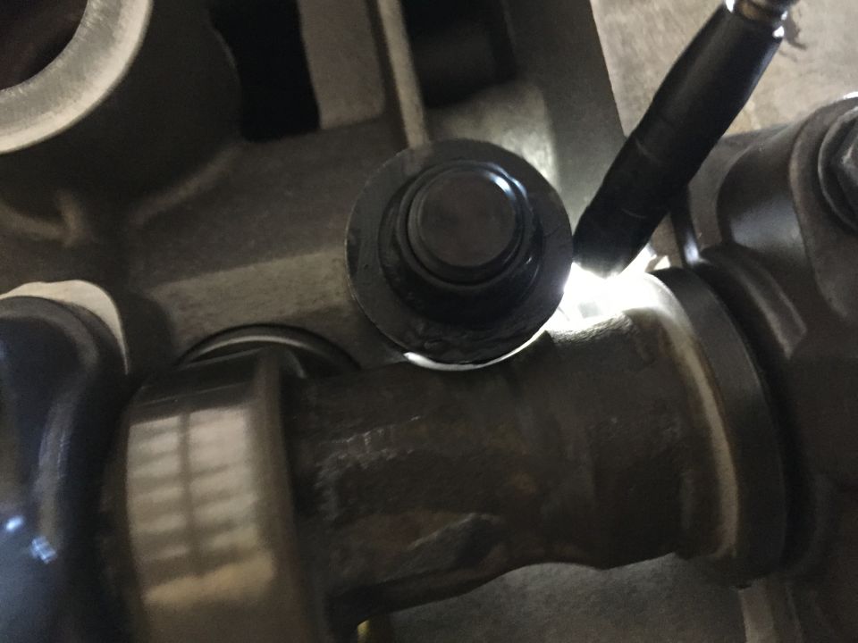 Close-up of a black circular component with a metal shaft, possibly a valve or sensor, within an engine block. A light illuminates the area