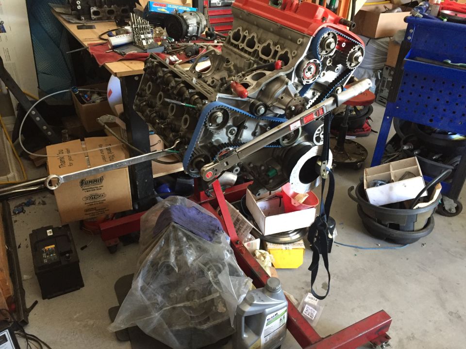 Engine on a red stand, with blue timing belts, in a cluttered garage