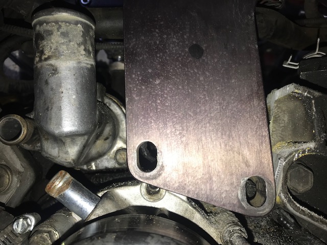 Close-up of engine components including a metal plate bolted over a thermostat housing