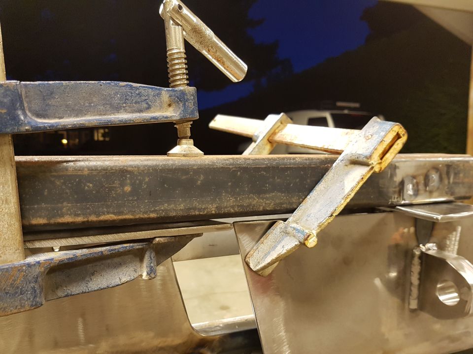 Clamps holding metal pieces together during fabrication. A white SUV is visible in the background