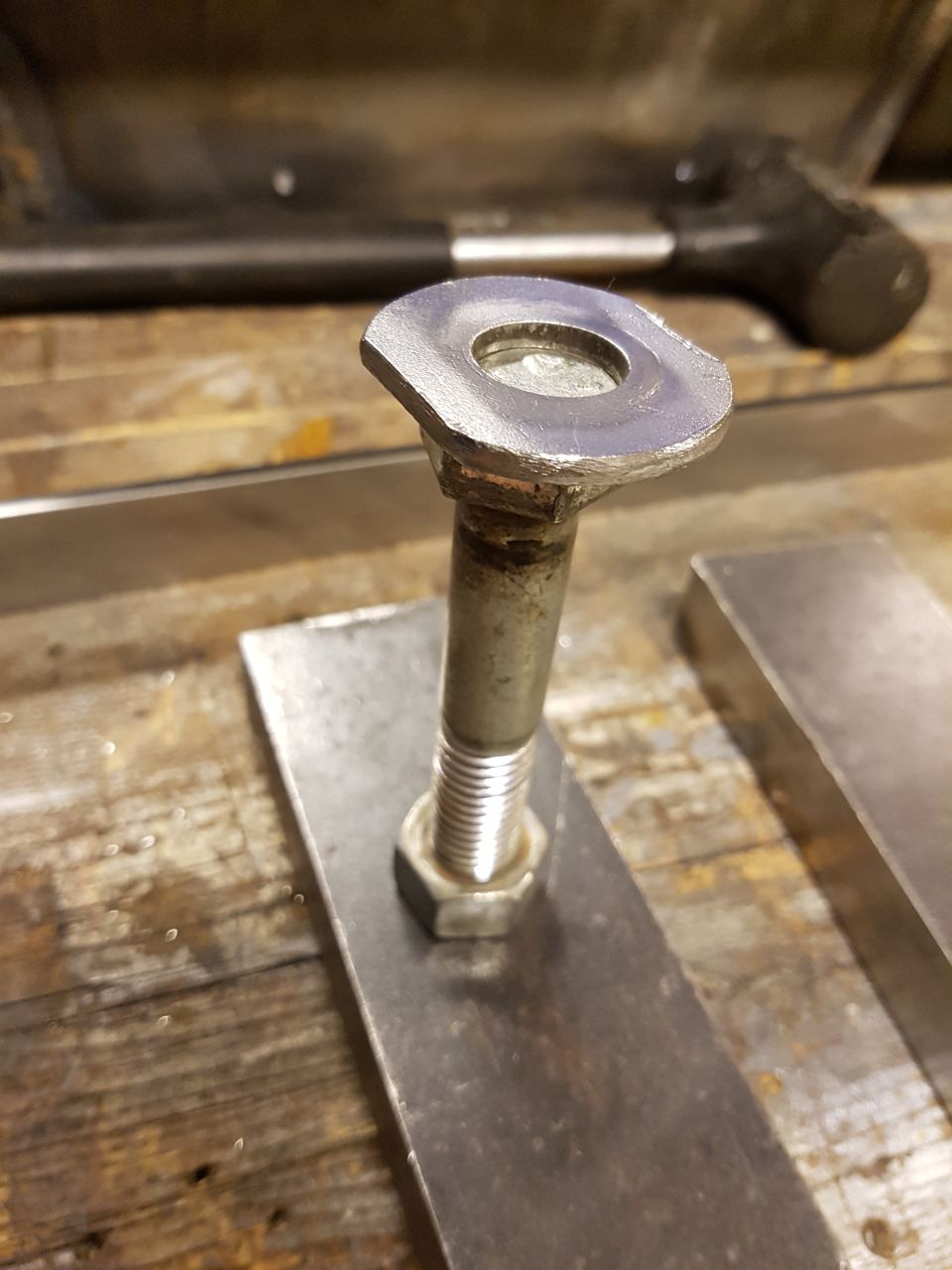Bolt with washer and nut securing metal plates, with a hammer in background