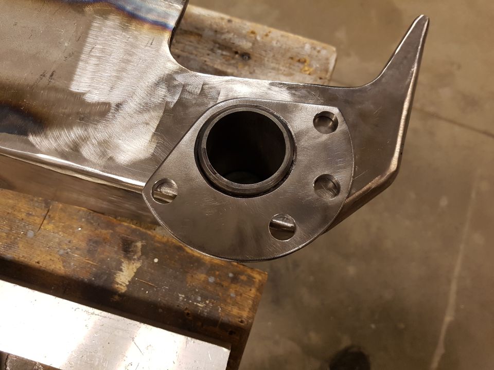 Close-up of a custom exhaust pipe flange with a circular opening and bolt holes, attached to a metal pipe
