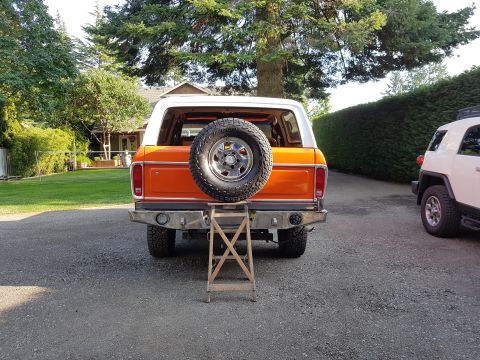 1978 Ford Bronco - Rear view of an orange 1978 Ford Bronco with a spare tire and custom bumper, parked next to another vehicle.