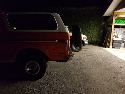 1978 Ford Bronco - Two vehicles parked outside a garage at night. The Bronco is in the foreground, with a white SUV behind it.