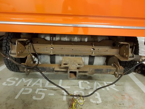 1978 Ford Bronco - The underside of an orange vehicle shows a trailer hitch and fuel tank assembly.