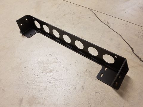 1978 Ford Bronco - A black metal bracket with multiple circular cutouts and mounting points sits on a concrete floor.
