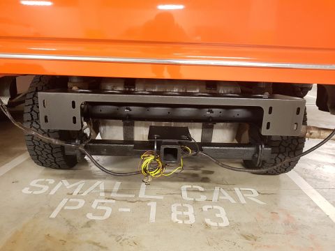 1978 Ford Bronco - The rear of an orange vehicle shows a trailer hitch and wiring, parked in a spot marked for small cars.