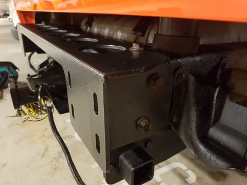 1978 Ford Bronco - Close-up of an aftermarket rear bumper and trailer hitch assembly, with wiring visible, attached to an orange vehicle.
