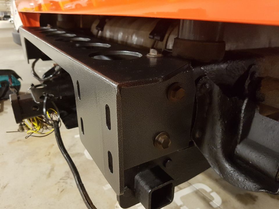 Orange vehicle body above black trailer hitch and bumper assembly with visible wiring