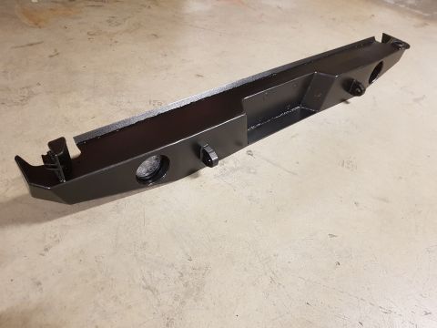 1978 Ford Bronco - This black aftermarket rear bumper features cutouts for lights and tow hooks, resting on a concrete surface.