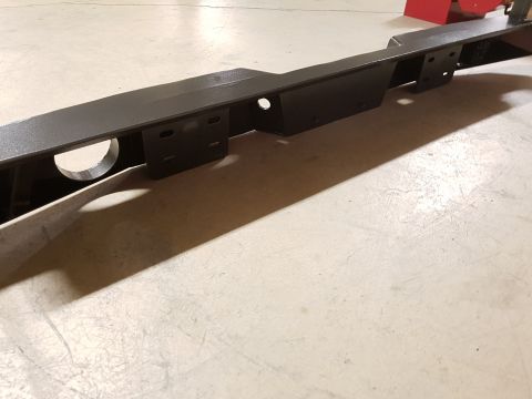 1978 Ford Bronco - A black metal frame part with mounting brackets and a circular cutout is shown on a concrete floor.