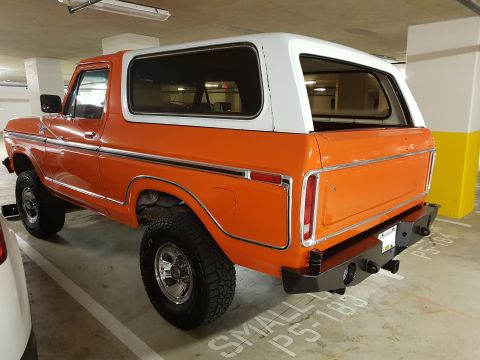 1978 Ford Bronco - This orange Ford Bronco is parked in a garage, showing its distinctive body style and white hardtop.