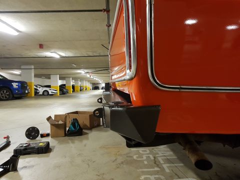 1978 Ford Bronco - Close-up of an orange vehicle's rear bumper and exhaust pipe in a parking garage.
