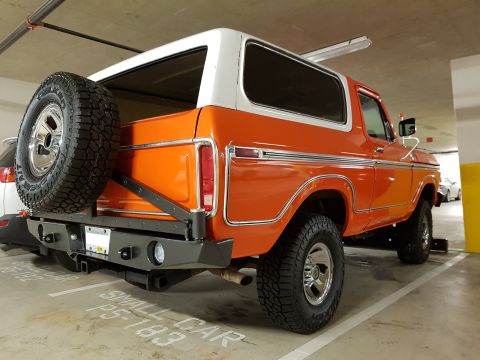 1978 Ford Bronco - Rear view of an orange and white Ford Bronco with a spare tire mounted on the tailgate.