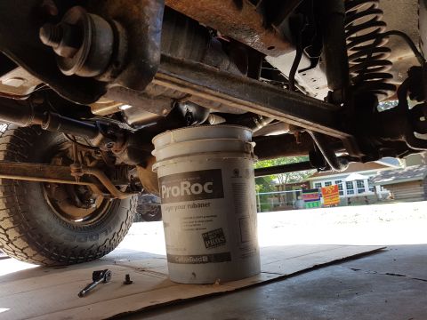 1978 Ford Bronco - The underside of a vehicle is shown with a bucket placed under the frame for support.