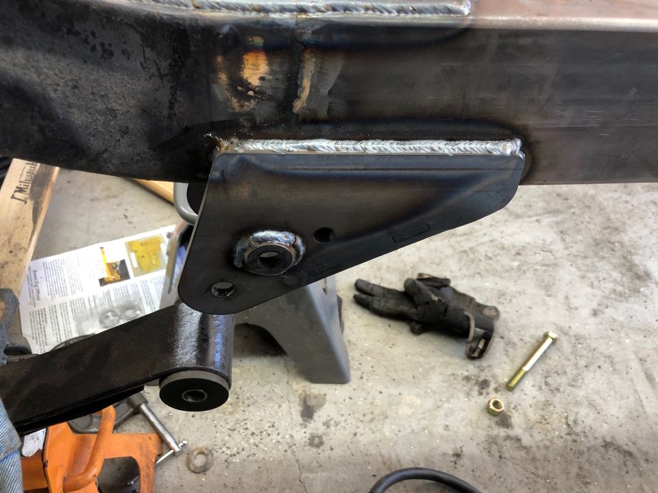 Close-up of vehicle frame with suspension bracket welded on. Jack stands and tools are visible
