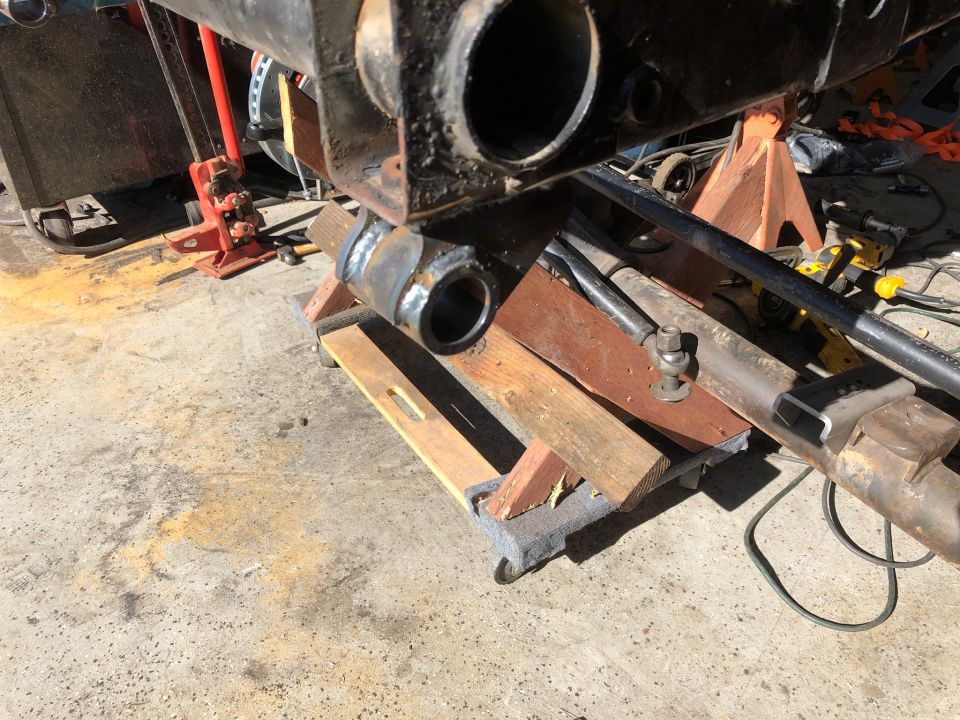 Vehicle suspension components on wooden blocks and jack stands, with welding visible