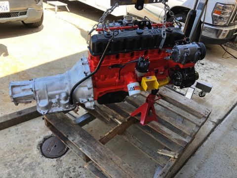 1992 Jeep Wrangler - A red and black engine assembly with a silver transmission is suspended by chains, supported by jack stands on a pallet.