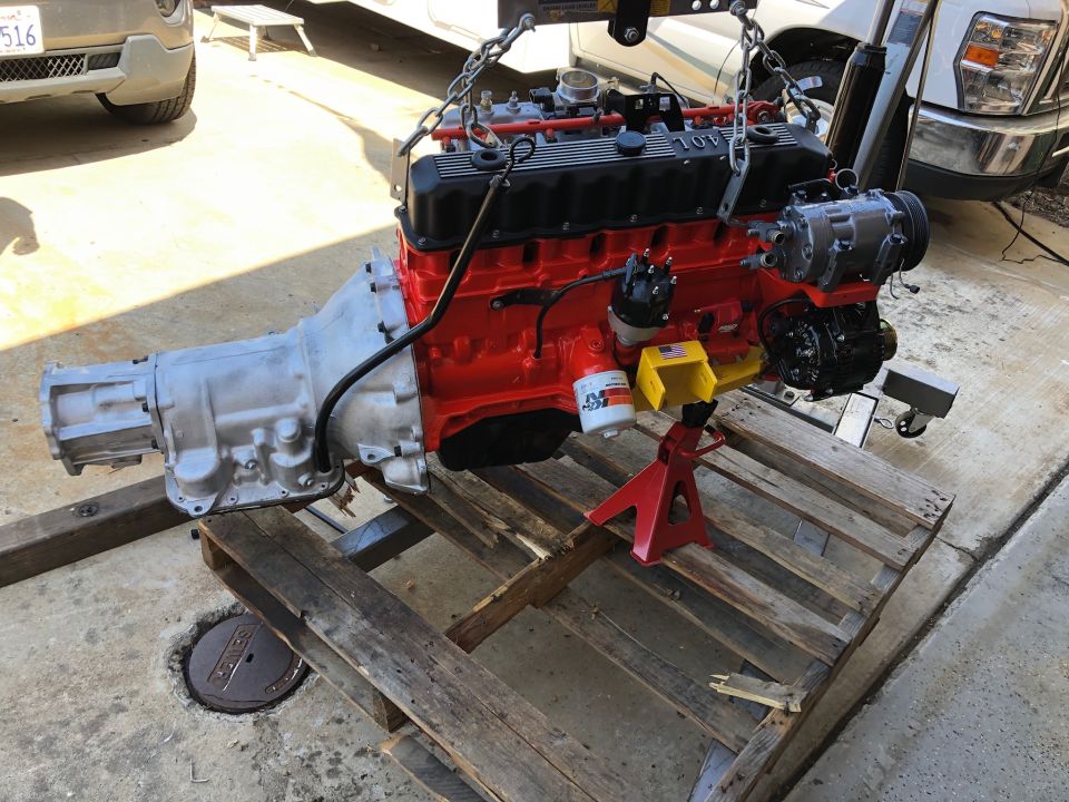 Engine and transmission assembly being lifted by chains, resting on a wooden pallet with jack stands