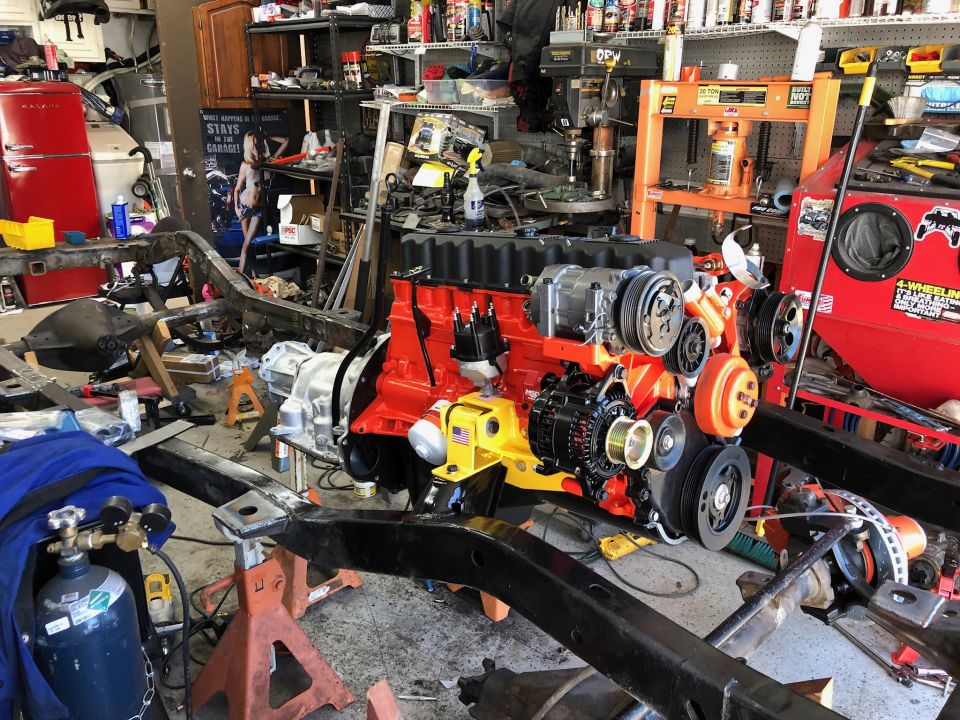 Rebuilt engine assembly with red block and orange accents, on stands in a cluttered garage
