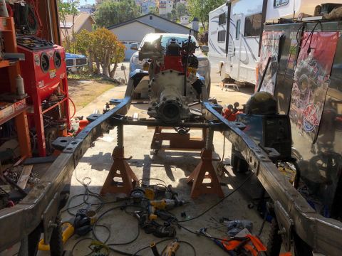 1992 Jeep Wrangler - The frame of a vehicle is supported by jack stands, with the engine assembly positioned above it.