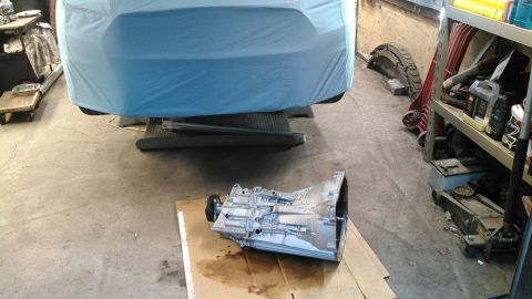 2017 Ford Mustang - A transmission sits on the floor next to a vehicle covered in a blue tarp in a garage setting.