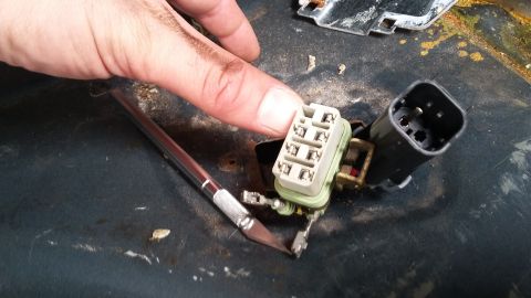 Close-up of a hand holding a tan electrical connector with exposed wires and a black connector nearby