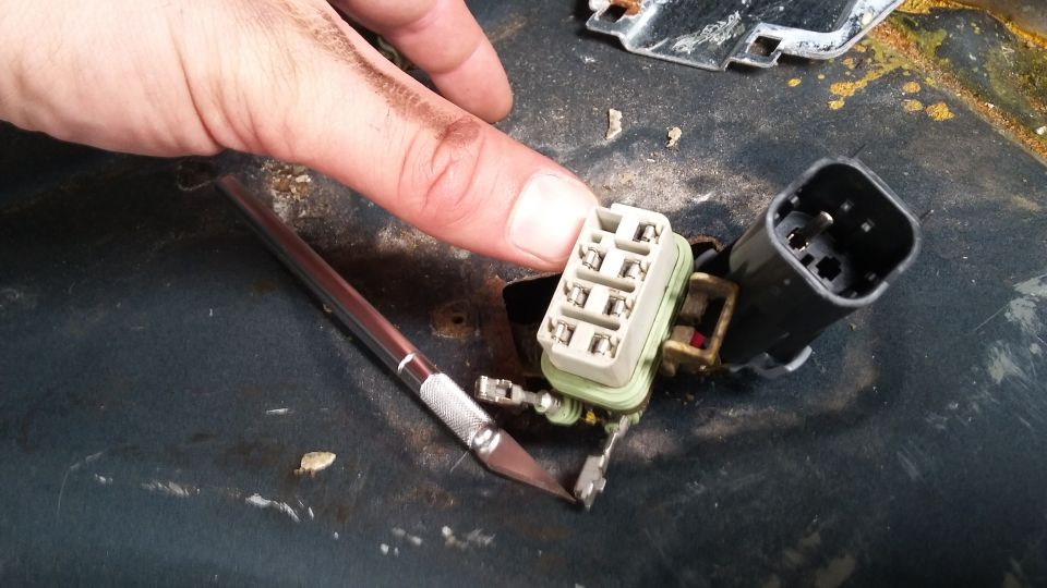 Close-up of a hand holding a tan electrical connector with exposed wires and a black connector nearby