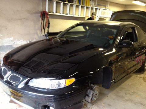 Black 2000 Pontiac Grand Prix coupe, front wheels removed, hood open, parked indoors