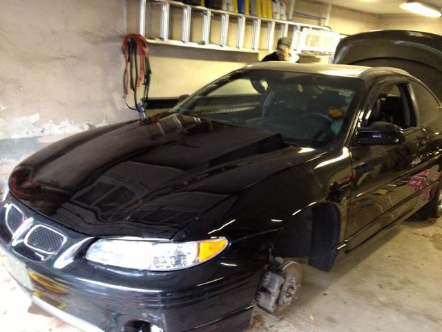 Black 2000 Pontiac Grand Prix coupe, front wheels removed, hood open, parked indoors