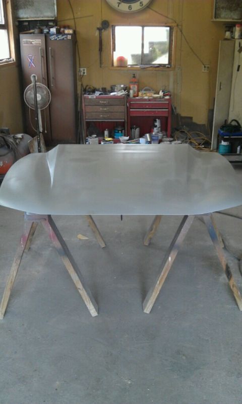 Car hood, unpainted, resting on wooden sawhorses in a workshop