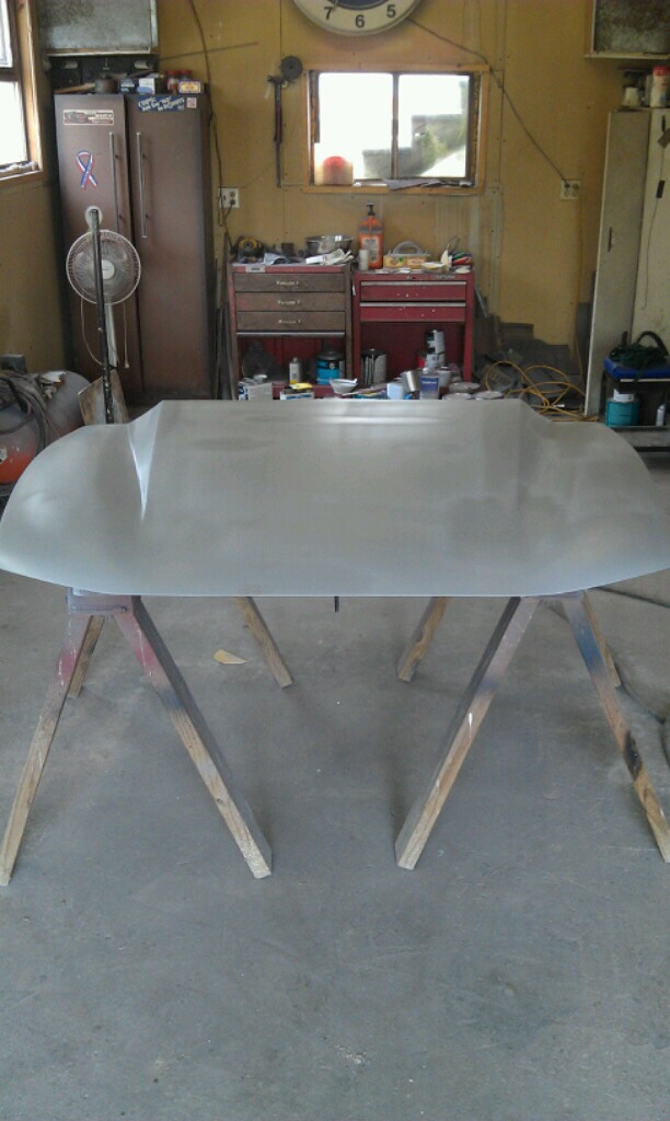 Car hood, unpainted, resting on wooden sawhorses in a workshop